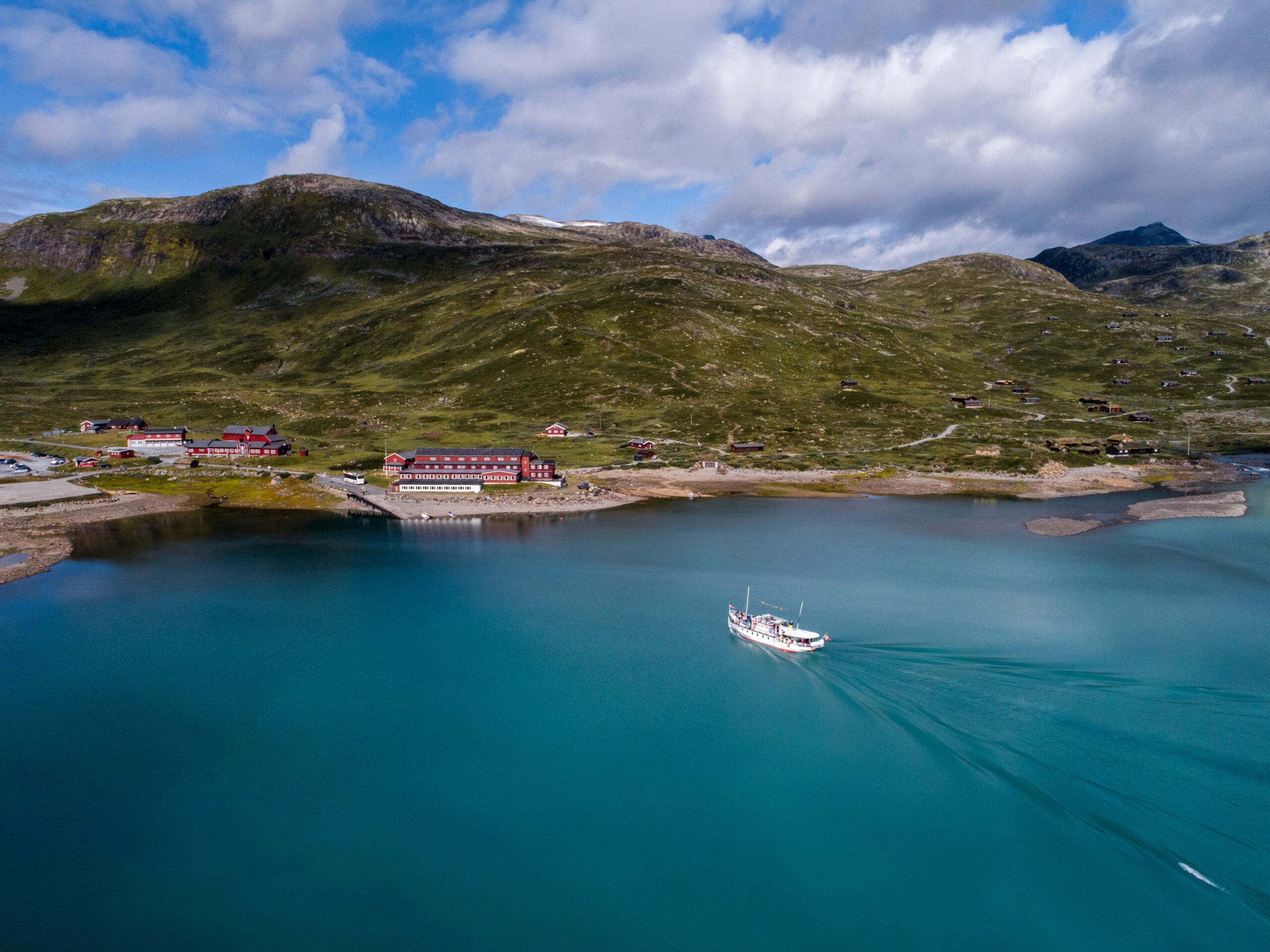 The boat Bitihorn on Bygdin closing in on Eidsbugarden and Fondsbu. Aerial footage.
